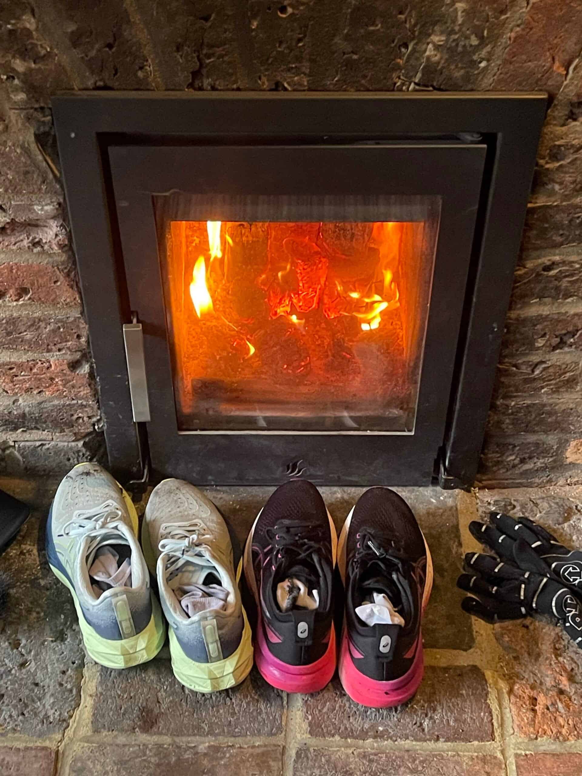 Three pairs of running shoes in front of a lit fireplace.