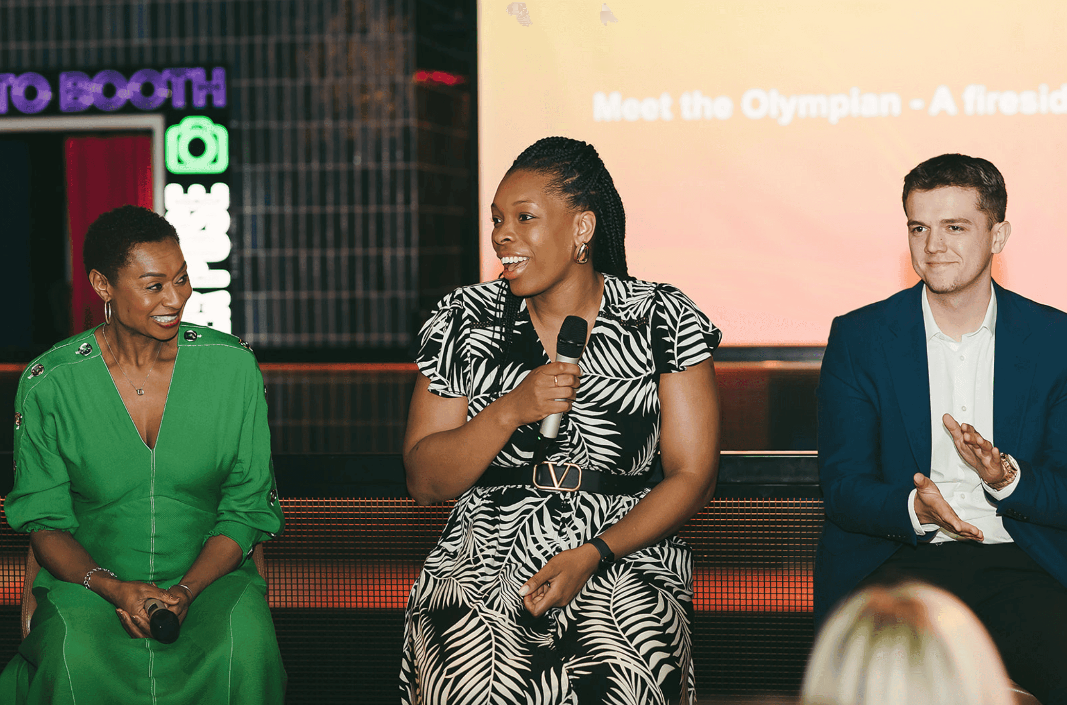 Three speakers on stage at a digital event, smiling and engaging with the audience.
