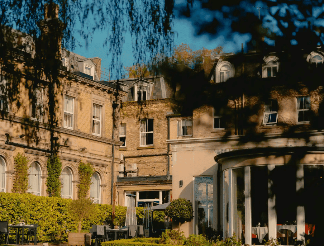 Historic building with garden and outdoor seating area under a blue sky.