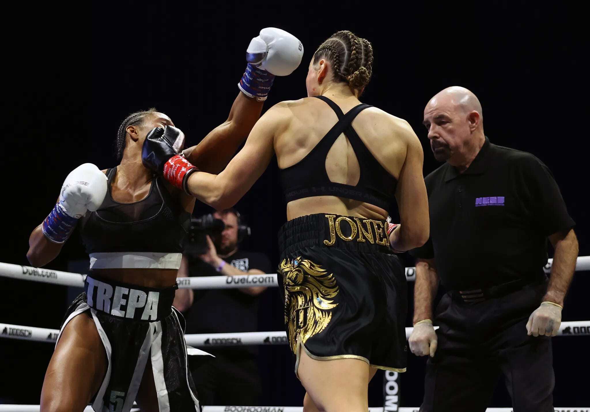 Two female boxers in a match with a referee observing closely.
