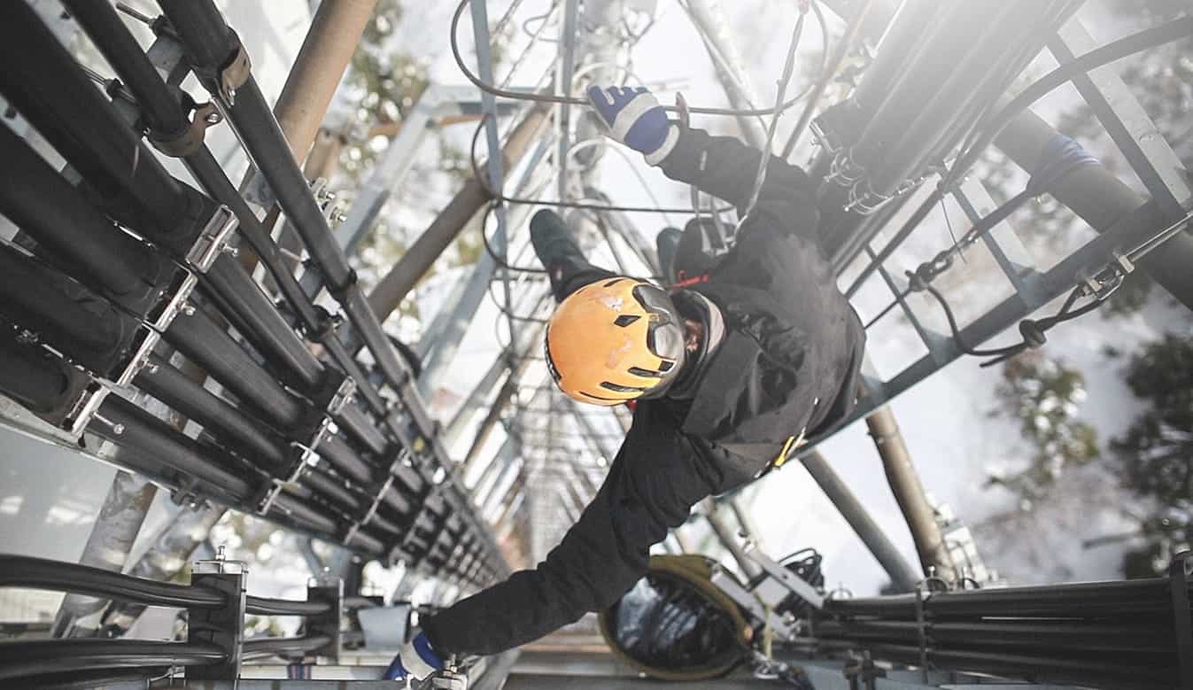 Worker in safety gear climbing telecommunications tower.